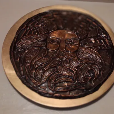 Sale Photo Thumbnail #69: Circular copper relief plaque depicting a stylized face with a flowing beard and hair, mounted on a brass backing.