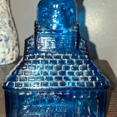 Sale Photo Thumbnail #118: Vintage T.C. Wheaton Co. cobalt blue glass bottle shaped like a house, featuring embossed brick patterns and company lettering.