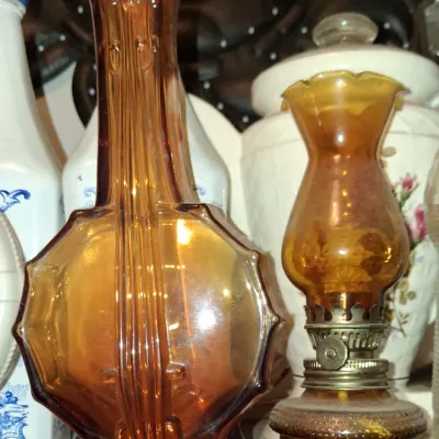 Sale Photo Thumbnail #61: Vintage amber glass violin-shaped bottle alongside a small amber glass miniature oil lamp, displayed with other collectible glassware.