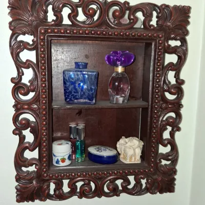 Sale Photo Thumbnail #31: Ornate carved dark wood shadow box wall shelf displaying various perfume bottles, small trinket boxes, and a miniature elephant figurine.
