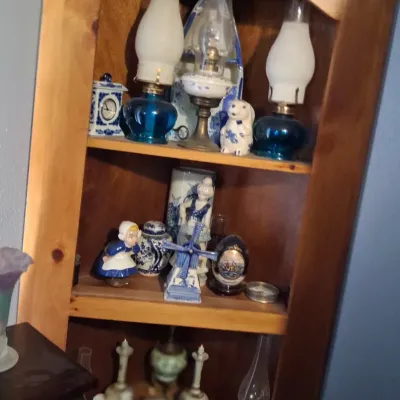 Sale Photo Thumbnail #100: Pine corner shelf unit filled with vintage collectibles, including blue glass hurricane lamps, Delftware-style figurines, and a miniature windmill.
