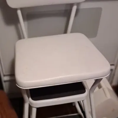 Sale Photo Thumbnail #84: Vintage Cosco-style white metal step stool chair with pull-out steps and vinyl padded seat and backrest.