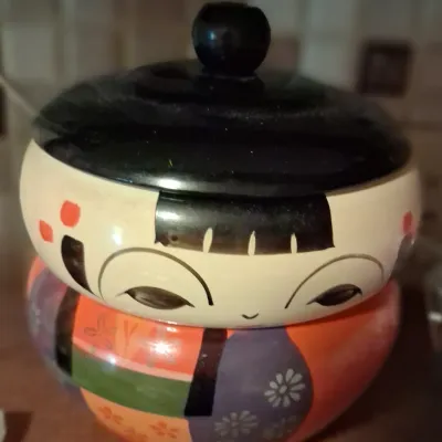 Sale Photo Thumbnail #76: Vintage Japanese Kokeshi doll-style ceramic lidded jar, featuring a hand-painted smiling face and colorful floral kimono details.