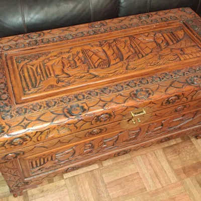 Sale Photo Thumbnail #144: Vintage hand-carved camphor wood chest featuring detailed relief carvings of sailing ships and floral borders, complete with a brass latch.