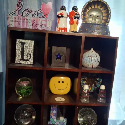 Sale Photo Thumbnail #101: Dark wood cubby shelf filled with various decorative items, including paperweights, a smiley face figurine, salt and pepper shakers, and celestial-themed decor.