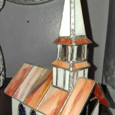 Sale Photo Thumbnail #128: Vintage stained glass church figurine featuring a white steeple, orange-toned roof, and blue arched windows.