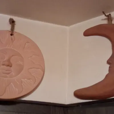 Sale Photo Thumbnail #82: Pair of terracotta wall plaques featuring a relief-carved sun and crescent moon with stylized faces, suspended by twine hangers.