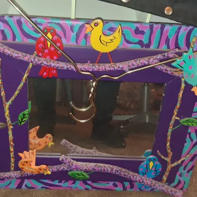 Sale Photo Thumbnail #10: Whimsical hand-painted wooden mirror frame decorated with colorful birds, branches, and abstract patterns in shades of purple, teal, and orange.