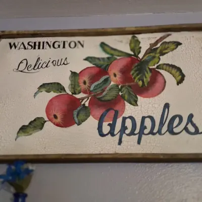 Sale Photo Thumbnail #94: Vintage-style wooden sign featuring a painted illustration of red apples with the text 'Washington Delicious Apples' on a crackled white background.