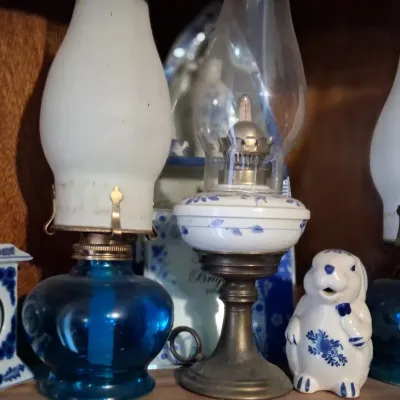 Sale Photo Thumbnail #104: Collection of vintage oil lamps, including a pair with blue glass bases and frosted white chimneys, alongside a Delft-style ceramic clock and rabbit figurine.