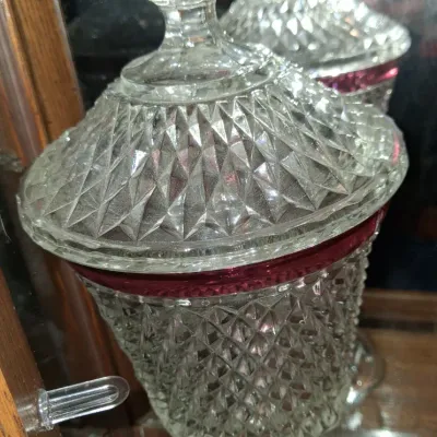 Sale Photo Thumbnail #139: Vintage diamond-cut pressed glass candy dish with a matching lid and a ruby red stained rim, displayed on a glass shelf.