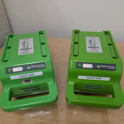 Sale Photo Thumbnail #233: Pair of Newcastle Systems green portable power pack batteries, showing active charge indicator lights and labeled "GOOD 2026".