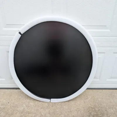 Sale Photo Thumbnail #65: Large circular black tabletop or sign blank, protected with white foam edge guards, leaning against a white garage door.
