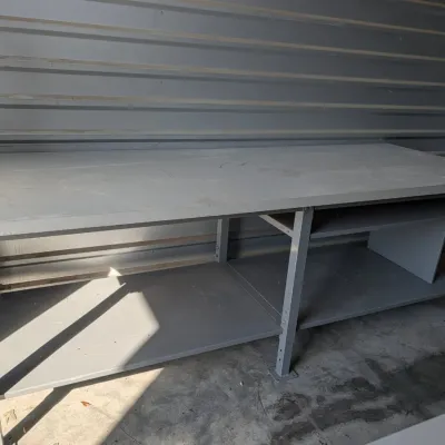 Sale Photo Thumbnail #54: Industrial gray metal workbench featuring a spacious work surface, lower storage shelves, and a built-in compartment.
