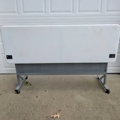 Sale Photo Thumbnail #182: Mobile flip-top training table with a white laminate surface, grey metal frame, and locking casters.