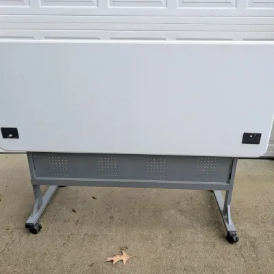 Sale Photo Thumbnail #180: Mobile flip-top training table with a white laminate top, grey metal base, and locking casters.