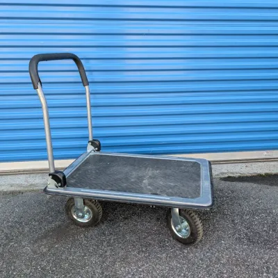 Sale Photo Thumbnail #4: Heavy-duty folding platform truck with a textured black non-slip deck, pneumatic tires, and a folding handle, showing light wear from use.