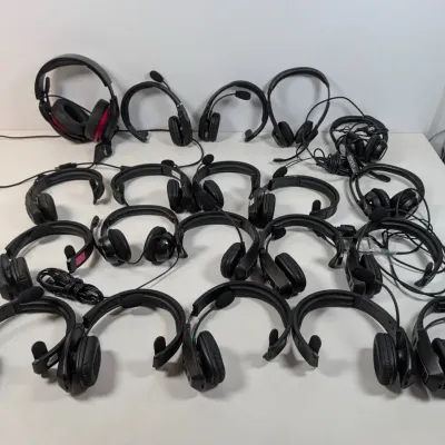 Sale Photo Thumbnail #305: Large collection of black over-ear headsets with attached microphones, arranged on a white tabletop.