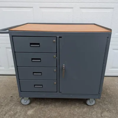 Sale Photo Thumbnail #71: Industrial gray metal rolling tool cart featuring a wooden work surface, four locking drawers, a large side cabinet, and a push handle.