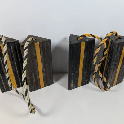 Sale Photo Thumbnail #132: Two pairs of heavy-duty rubber wheel chocks, each pair connected by a rope handle and featuring yellow reflective safety stripes.