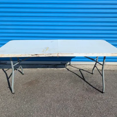 Sale Photo Thumbnail #61: White plastic folding utility table with grey metal legs, showing some surface wear and staining.