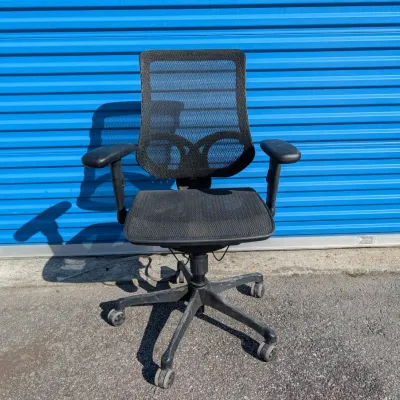 Sale Photo Thumbnail #55: Black mesh ergonomic office chair with adjustable armrests and a five-star caster base, showing some dust and wear from use.
