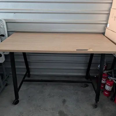 Sale Photo Thumbnail #12: Modern industrial-style desk featuring a light wood laminate top on a black metal frame with caster wheels.