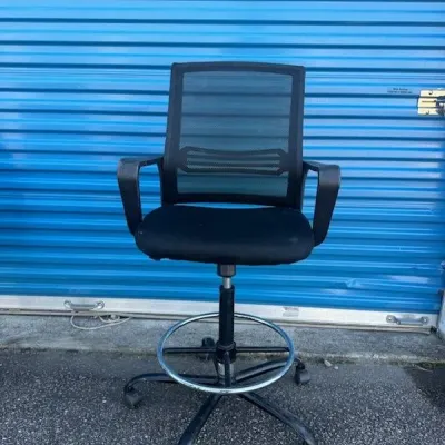 Sale Photo Thumbnail #27: Modern black mesh drafting chair with adjustable height, armrests, and a circular chrome footrest on a wheeled base.