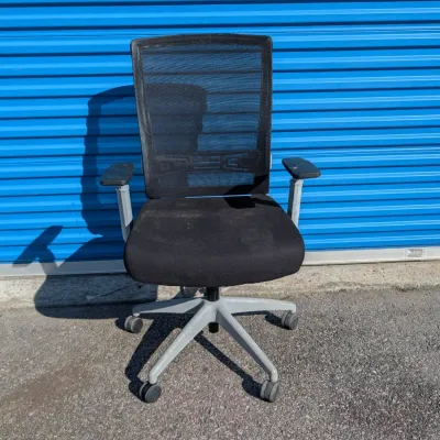 Sale Photo Thumbnail #56: Modern black mesh office chair with adjustable armrests and a grey five-star rolling base, showing some light wear on the seat cushion.