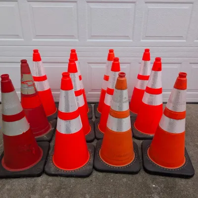 Sale Photo Thumbnail #185: Group of twelve orange and red traffic cones with reflective white stripes, showing varying degrees of wear.