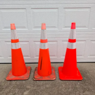 Sale Photo Thumbnail #184: Three orange traffic cones with reflective silver stripes, showing some wear and scuffs from use.