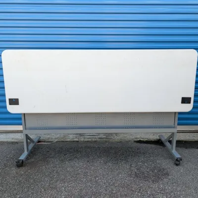 Sale Photo Thumbnail #18: Mobile flip-top training table with a white laminate surface, grey metal frame, and locking casters.