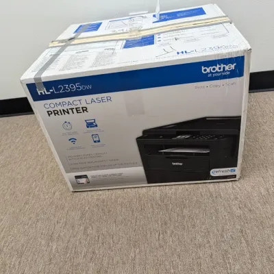 Sale Photo Thumbnail #221: Brother HL-L2395DW compact laser printer, in its original box with tape sealing the top.