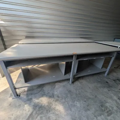 Sale Photo Thumbnail #49: Industrial gray metal workbenches with built-in lower shelving, showing some wear from use.