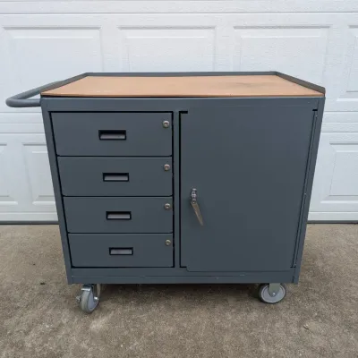 Sale Photo Thumbnail #73: Industrial gray metal rolling tool cart featuring four locking drawers, a large side cabinet, a push handle, and a wooden work surface.