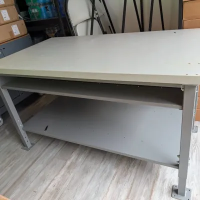 Sale Photo Thumbnail #183: Industrial-style workbench featuring a thick laminate top, a sturdy grey metal frame with adjustable-height legs, and a lower storage shelf.