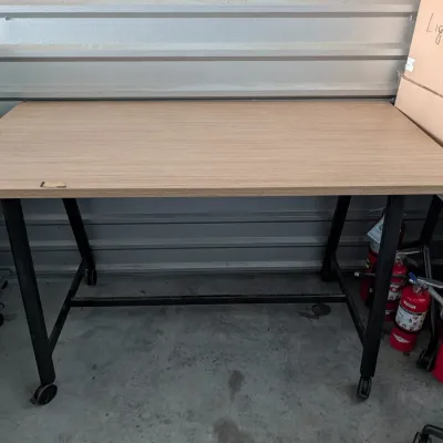 Sale Photo Thumbnail #11: Modern light oak laminate desk with a black metal frame on casters, showing minor wear on the front edge.