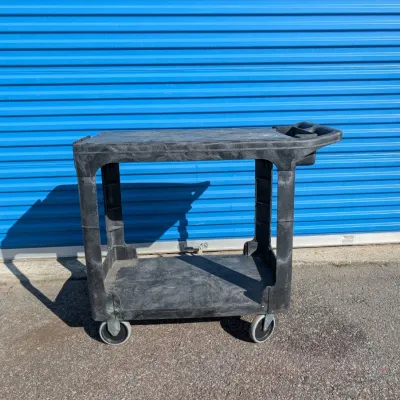 Sale Photo Thumbnail #63: Heavy-duty black plastic utility cart with two shelves, integrated handle, and swivel casters, showing some wear from use.