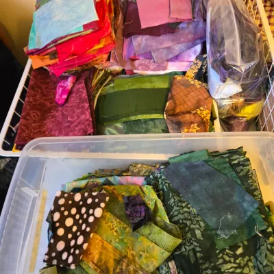 Assorted quilting fabric scraps and fat quarters in various colors and patterns, organized in plastic bins and wire baskets.