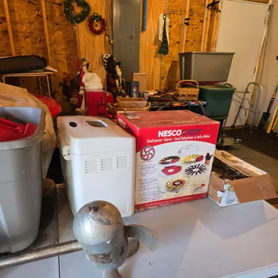 Sale Photo Thumbnail #78: Nesco Snackmaster Entrée food dehydrator in its original box, displayed alongside a white breadmaker and a vintage metal boat propeller on a folding table.