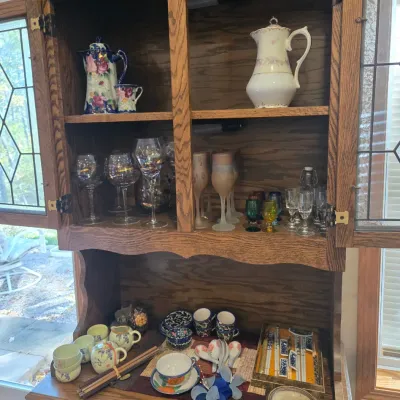 Sale Photo Thumbnail #50: Vintage oak hutch featuring leaded glass doors, filled with an assortment of glassware, teacups, and decorative porcelain pieces.