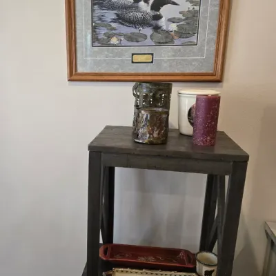 Sale Photo Thumbnail #43: Framed loon print in a wooden frame hanging above a dark wood nesting table set displaying candles, a ceramic jar, and decorative trays.