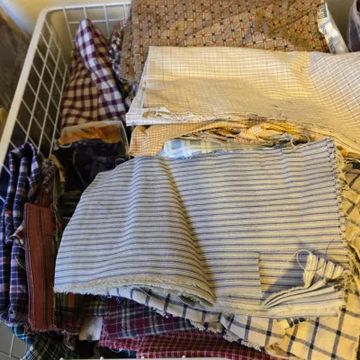 Assorted fabric remnants and quilting scraps in various plaid, striped, and patterned designs, stored in a white wire basket.