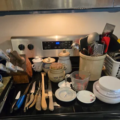 Sale Photo Thumbnail #71: Assorted kitchenware including a wooden knife block with knives, ceramic canisters, a crock filled with utensils, a glass measuring cup, and a kitchen scale.
