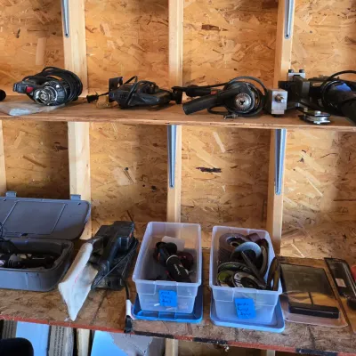 Sale Photo Thumbnail #110: Assorted power tools and accessories, including a corded drill, jigsaw, rotary tool in a hard case, and plastic bins containing grinding wheels and sanding discs.
