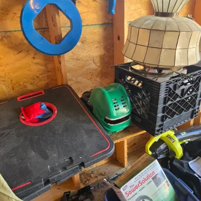 Sale Photo Thumbnail #99: Assorted garage and household items, including a vintage slag glass style lamp shade, a portable cornhole game set, a Ryobi leaf blower, and various tools.