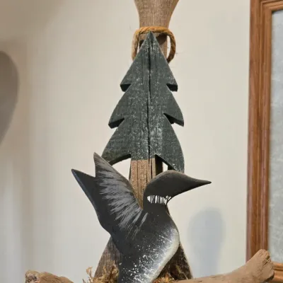 Sale Photo Thumbnail #35: Rustic folk art wooden sculpture featuring a painted loon and pine tree mounted on a weathered paddle and driftwood base with moss accents.