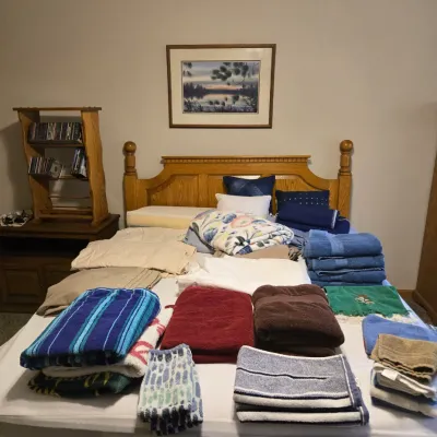 Sale Photo Thumbnail #54: Assorted household linens, including bath towels, hand towels, and sheets, displayed on a wooden queen-size bed frame with a matching headboard.