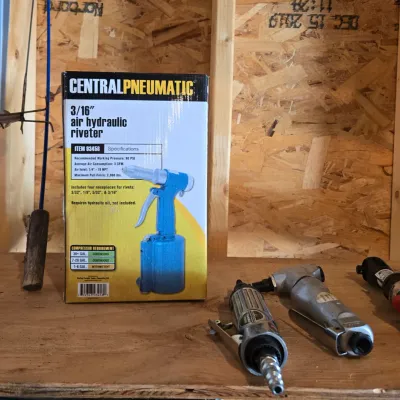 Sale Photo Thumbnail #113: Central Pneumatic 3/16-inch air hydraulic riveter in its original box, shown alongside various pneumatic hand tools on a wooden workbench.