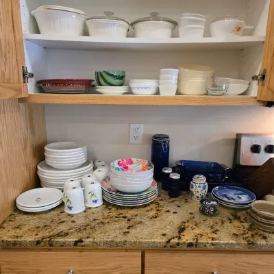 Sale Photo Thumbnail #72: Assorted kitchenware including CorningWare casserole dishes, Corelle bowls, floral melamine plates, and various ceramic mugs and canisters.